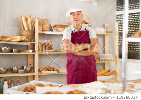 Smiling elderly baker standing with crossed arm in bakery Smiling elderly baker standing with crossed arm in bakery 119260317
