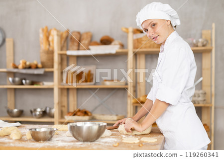 Adolescence girl baker works with rolling pin, rolls out and spreads out pieces of dough 119260341