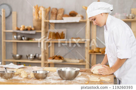 Young female baker kneading dough in small bakery 119260393