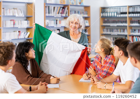 Mature female teacher shows scholchildren the national flag of Italy Mature female teacher shows scholchildren the national flag of Italy 119260452