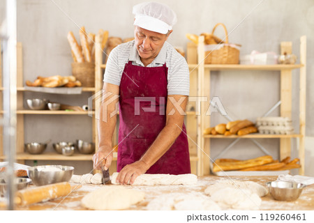 Elderly baker shapes raw dough into baguette Elderly baker shapes raw dough into baguette 119260461