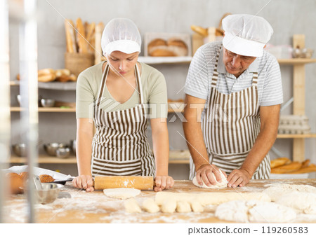 Man and woman bakers roll out dough with rolling pin Man and woman bakers roll out dough with rolling pin 119260583