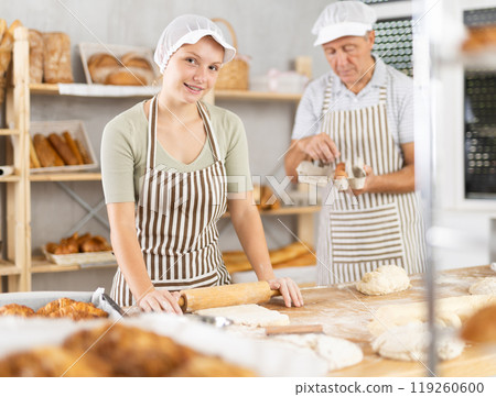 Adolescence girl baker works with rolling pin, rolls out and spreads out pieces of dough Adolescence girl baker works with rolling pin, rolls out and spreads out pieces of dough 119260600