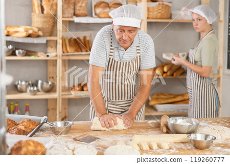 Skilled elderly baker kneading dough in cozy artisan bakery 119260777