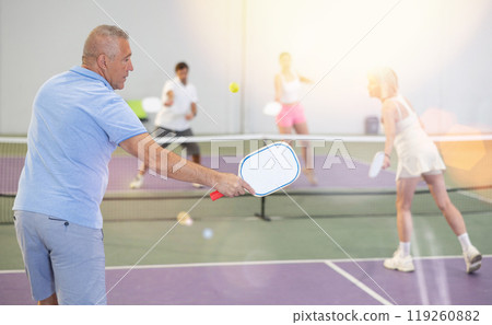 Rear view of man with white racket playing pickleball tennis at court 119260882