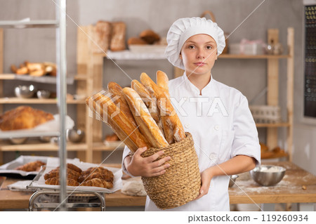 Young female baker with basket of baguettes Young female baker with basket of baguettes 119260934