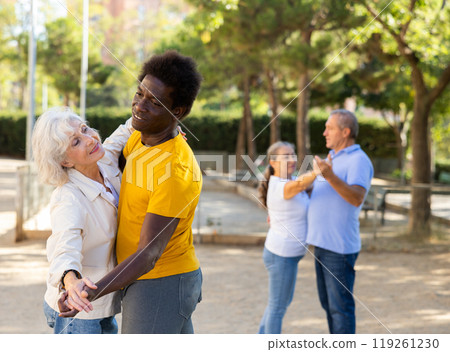 Happy positive mature multinational pensioners spending time together and dancing in pairs outdoors 119261230