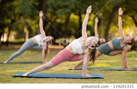 Yoga lesson visitors girls perform Utthita Parshvakonasana in park Yoga lesson visitors girls perform Utthita Parshvakonasana in park 119261315