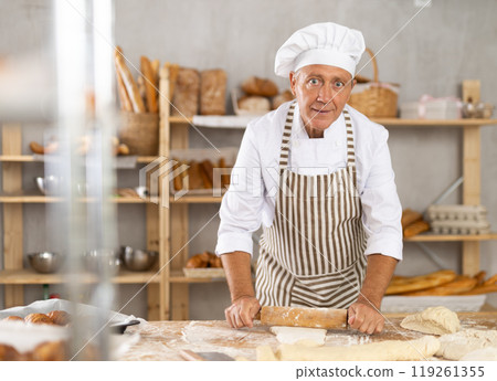 Elderly man rolls out dough with rolling pin Elderly man rolls out dough with rolling pin 119261355