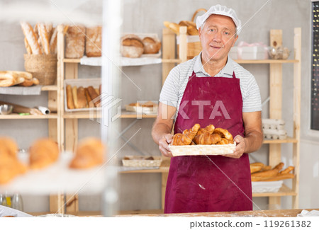 Smiling elderly baker offering freshly baked croissants 119261382