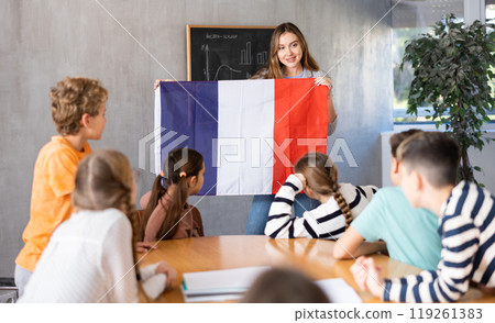 Geography lesson in school class - teacher talks about France, holding flag in his hands 119261383