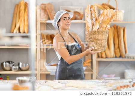 Young saleswoman displays baguettes in wicker basket 119261575