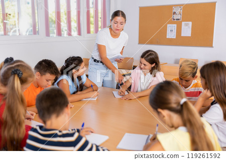 Kids sitting around desk in classroom and studying during lesson Kids sitting around desk in classroom and studying during lesson 119261592