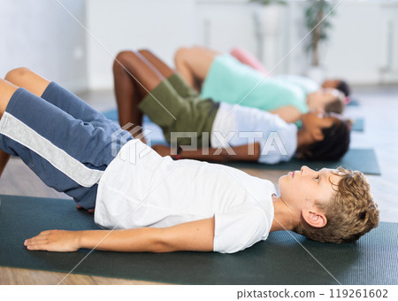 In sport studio with group of friends, boy perform bridge pose, setu bandha sarvangasana 119261602