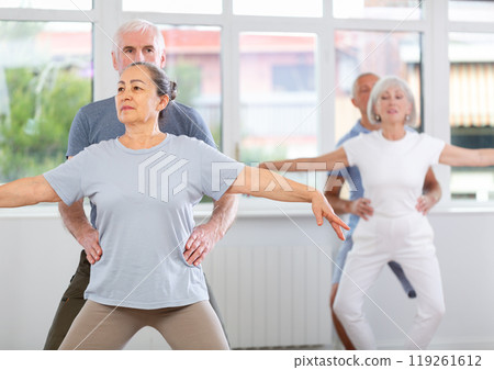 Mature woman practicing plie position in pair with man in dance studio Mature woman practicing plie position in pair with man in dance studio 119261612