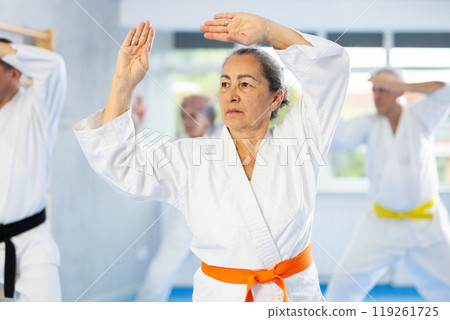 Old woman attendee of karate classes practicing kata standing in row with others 119261725