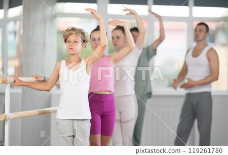 Group of teenagers stand in third position near ballet barre during group training in dance studio 119261780