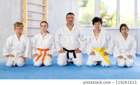 Children in white kimono sitting on knees on tatami in sport gym 119261813