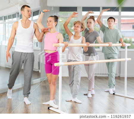 Girls and boys in ballet class perform third position under male teacher guidance. 119261937