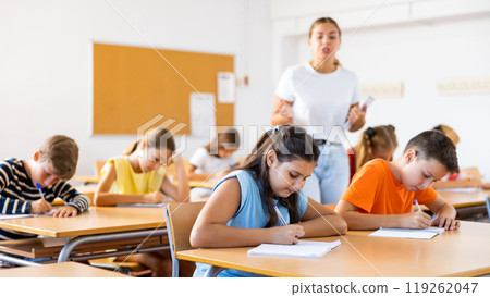 School kids with pens and notebooks studying in classroom with teacher 119262047