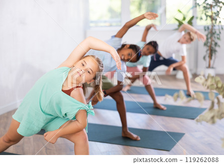 Children standing in Parivrtta Trikonasana or Revolved Triangle Pose on mats during group yoga training in fitness center 119262088