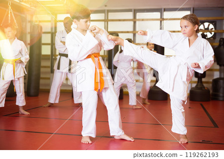 Children practicing in pair karate movements with male trainer supervision Children practicing in pair karate movements with male trainer supervision 119262193