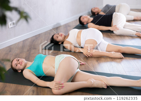 Slim young girl practicing revolved abdomen pose of yoga on black mat 119262335