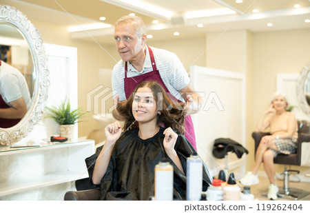 Cheerful girl client discussing new hairstyle with elderly male hairdresser 119262404