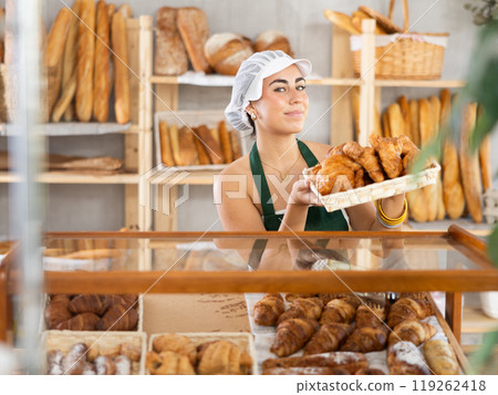 Young saleswoman displays croissants in square wicker basket 119262418
