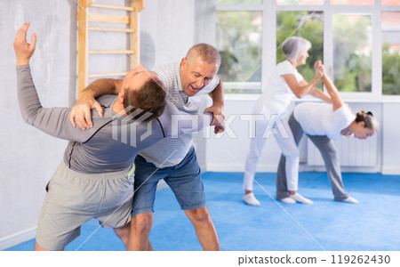 Mature man at self-defense lesson learns how to make painful blows with his hand and foot 119262430