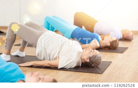 Group of young mature old people in sportswear exercising Pilates while lying on mats in rehabilitation center 119262528