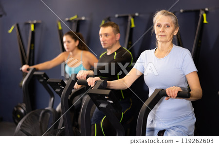 Aged woman doing cardio workout on exercise bike in gym Aged woman doing cardio workout on exercise bike in gym 119262603