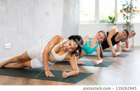Yoga class of sporty women in activewear performing Halasana or Plow Pose on mats during workout in yoga studio 119262945
