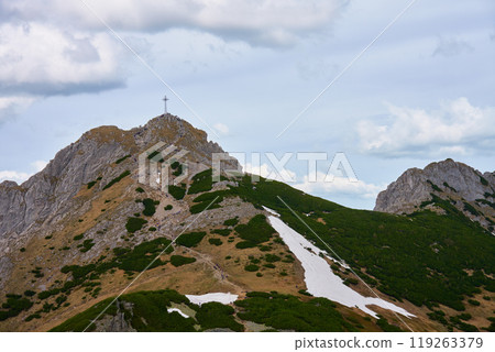 Rugged hiking trail leading to mountain summit with large cross under cloudy sky. Tatra mountains in Zakopane, Poland. Giewont mountain summit. Natural landscape Rugged hiking trail leading to mountain summit with large cross under cloudy sky. Tatra mountains in Zakopane, Poland. Giewont mountain summit. Natural landscape 119263379