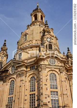 Buiilding exterior of Dresden Frauenkirche. Baroque architecture with stonework, large arched windows and grand dome under a clear sky 119263382