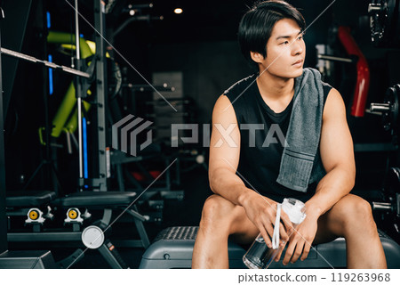 Portrait of Asian young man trained body in black sportswear sitting for rest holding water or protine in fitness gym, Weight training, healthy lifestyle concept Portrait of Asian young man trained body in black sportswear sitting for rest holding water or protine in fitness gym, Weight training, healthy lifestyle concept 119263968