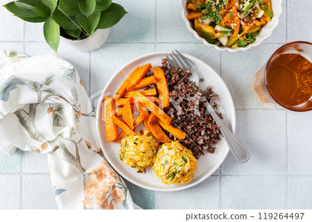 A delicious and wholesome plate featuring brown rice, sweet potatoes, and chickpea pancakes made with squash, perfect for a balanced and nutritious meal, fresh salad of tomatoes and cucumbers 119264497
