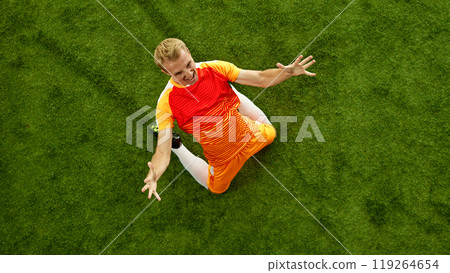Kneeling in celebration, footballer's joy unmistakable. Triumph of victory clear as he raises his arms, relishing success of his play. 119264654