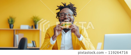 Joyful African-American man in vibrant yellow suit enjoying burger at his office desk. Energetic, fun mood. 119264716