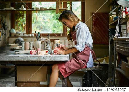 Female artist decorating and painting handmade ceramic clay cup at her creative workshop 119265957