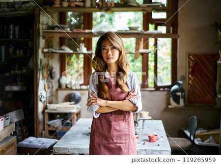 Successful female artist posing at creative workshop with her artwork in the background Successful female artist posing at creative workshop with her artwork in the background 119265959