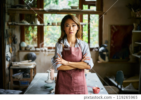 Successful female artist posing at creative workshop with her artwork in the background Successful female artist posing at creative workshop with her artwork in the background 119265965