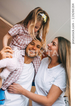 Loving family enjoys playful moment indoors with their daughter in casual attire 119266164