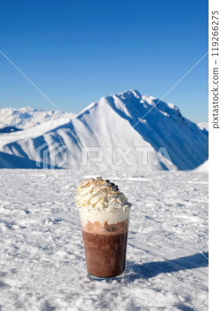 A glass of coffee with whipped cream against the backdrop of snow-capped mountains on a sunny day A glass of coffee with whipped cream against the backdrop of snow-capped mountains on a sunny day 119266275