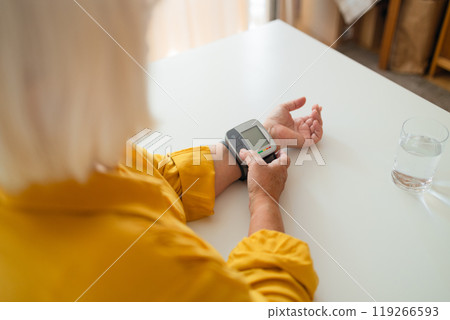 Senior woman with hypertension measuring blood pressure herself at home. Glass of water on the table 119266593