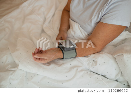Close up of woman checks her blood pressure, a tonometer is worn on her wrist in a bed. Medical device for measuring blood pressure and heart rate used at hand wrist 119266632