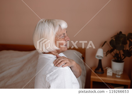 Elderly woman shoulder pain osteochondrosis. Senior woman with shoulder pain on a bed at home office Elderly woman shoulder pain osteochondrosis. Senior woman with shoulder pain on a bed at home office 119266653