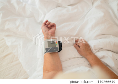 Close up of woman checks her blood pressure, a tonometer is worn on her wrist in a bed. Medical device for measuring blood pressure and heart rate used at hand wrist 119266659