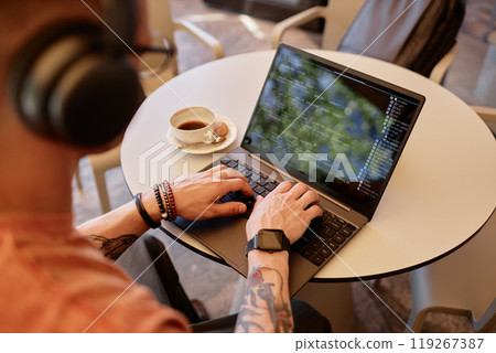 Over shoulder shot of male IT developer writing code on laptop sitting at cafe table with cup of coffee at hand during coffee break or lunch, copy space 119267387