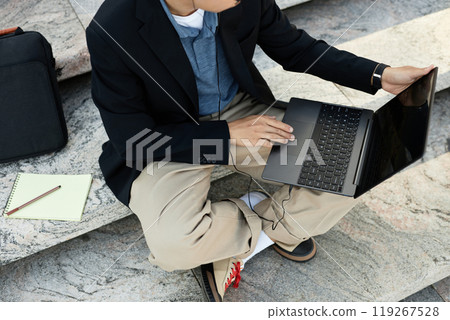 Cropped shot of unrecognizable IT programmer using laptop to work keeping fingers on touchpad while writing code sitting on concrete steps outside in street, copy space 119267528